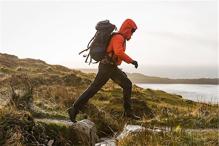 A man with a rucksack and winter clothing leaping across a small stream in an open exposed landscape. Stock Photo - Premium Royalty-Free, Code: 6118-08399673