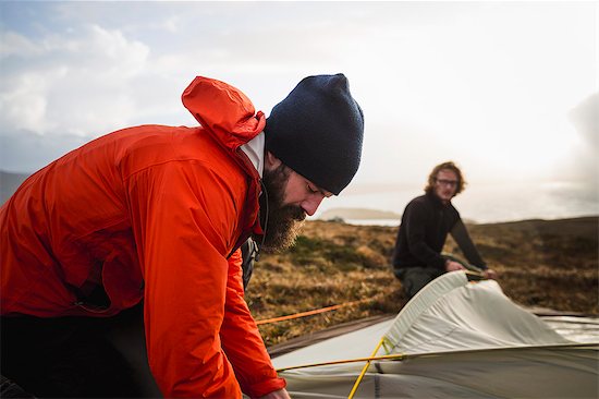 Two men holding and putting up a small tent in open space. Wild camping. Stock Photo - Premium Royalty-Free, Image code: 6118-08399679