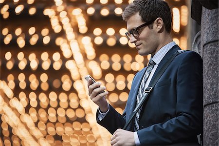A working day. Businessman in a work suit and tie on a city street, checking his phone. Stock Photo - Premium Royalty-Free, Code: 6118-08399600