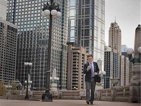 A working day. Businessman in a work suit and tie on a city street, checking his phone. Stock Photo - Premium Royalty-Free, Code: 6118-08399604