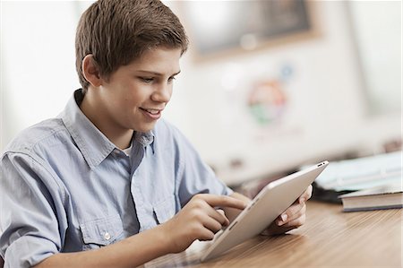 simsearch:6118-08351907,k - A boy sitting at a desk using a digital tablet. Fotografie stock - Premium Royalty-Free, Codice: 6118-08399630