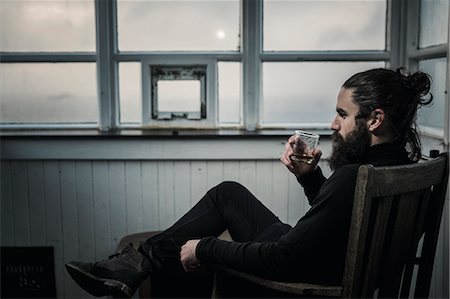 A man sitting looking at the view out of a window, drinking from a glass. Photographie de stock - Premium Libres de Droits, Code: 6118-08399702