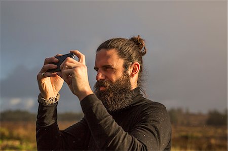 simsearch:6118-08399692,k - A man standing using a smart phone to take a photograph under a grey sky. Foto de stock - Sin royalties Premium, Código: 6118-08399713