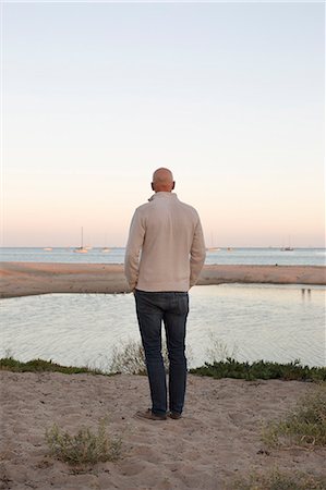 simsearch:6118-08991633,k - Bald man standing on a sandy beach by the ocean. Stock Photo - Premium Royalty-Free, Code: 6118-08313698