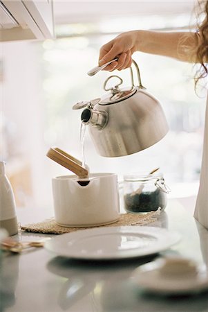 Woman standing in a kitchen pouring hot water from a kettle into a tea pot. Stock Photo - Premium Royalty-Free, Code: 6118-08313742