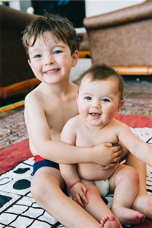 sister hugs baby - Two siblings, a boy and his baby sister sitting on a rug laughing. Stock Photo - Premium Royalty-Free, Code: 6118-08313828