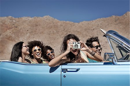 simsearch:6118-08488203,k - A group of friends in a pale blue convertible on the open road, driving across a dry flat plain surrounded by mountains. Stock Photo - Premium Royalty-Free, Code: 6118-08488177
