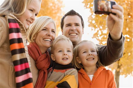 A family of two parents and three children posing for a selfy under the autumn leaves on the trees. Stock Photo - Premium Royalty-Free, Code: 6118-08488373
