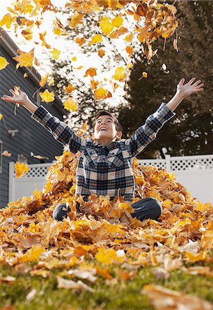 simsearch:6118-08971638,k - A young boy playing in a huge pile of raked autumn leaves. Photographie de stock - Premium Libres de Droits, Code: 6118-08488381