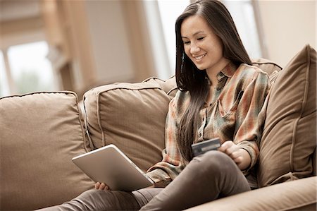 simsearch:6118-07966891,k - A woman sitting on a sofa at home holding a digital tablet and a credit card, shopping online. Photographie de stock - Premium Libres de Droits, Code: 6118-08488386