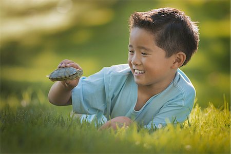 A boy lying on the grass holding a small terrapin or turtle. Photographie de stock - Premium Libres de Droits, Code: 6118-08488334