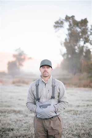 simsearch:6118-08488428,k - A fisherman standing with hands in his pockets in the dawn light. Stock Photo - Premium Royalty-Free, Code: 6118-08488422