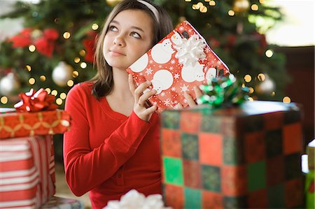 A girl by a Christmas tree shaking a present trying to guess what it is. Foto de stock - Sin royalties Premium, Código: 6118-08521642