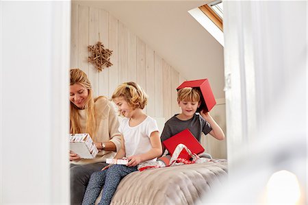 family christmas blond not outdoors - Christmas morning in a family home. A mother and two children sitting on a bed opening presents. Foto de stock - Sin royalties Premium, Código: 6118-08521741