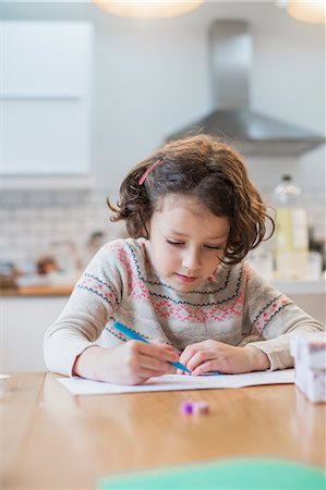 A girl sitting at a kitchen table writing a card or letter. Stock Photo - Premium Royalty-Free, Code: 6118-08521745