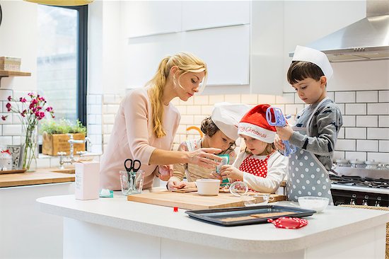A woman and three children working together, making a gingerbread house, and icing the gingerbread. Stock Photo - Premium Royalty-Free, Image code: 6118-08521749