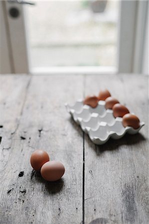 Fresh hen's eggs in a box and on a wooden table. Photographie de stock - Premium Libres de Droits, Code: 6118-08521776