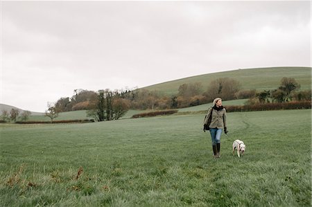 simsearch:6118-07731937,k - A woman walking with a dog across a grass field. Photographie de stock - Premium Libres de Droits, Code: 6118-08521795