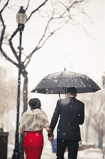 A woman in a long red evening dress and a man in a suit, walking through snow in the city. Stock Photo - Premium Royalty-Free, Image code: 6118-08521890