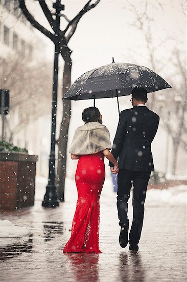 A woman in a long red evening dress with fishtail skirt and a fur stole, and a man in a suit, walking through snow in the city. Photographie de stock - Premium Libres de Droits, Le code de l’image : 6118-08521891