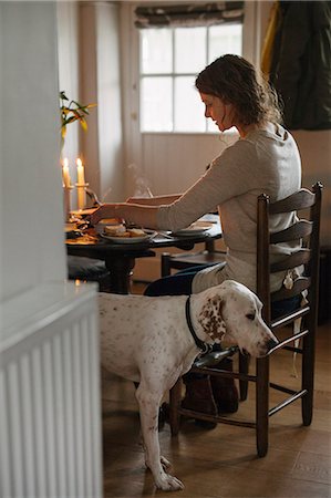 A woman seated at a table in a ladderback chair, a large white dog beside her. Photographie de stock - Premium Libres de Droits, Code: 6118-08521803