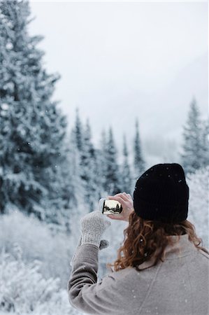 A woman using a smart phone, photographing pine forests in snow, Stock Photo - Premium Royalty-Free, Code: 6118-08521811