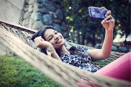 A woman lying in a garden hammock taking selfies with her phone. Stock Photo - Premium Royalty-Free, Code: 6118-08521951