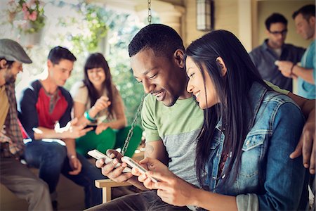 A group of friends, men and women at a house party, a couple checking their smart phones. Stock Photo - Premium Royalty-Free, Code: 6118-08521900