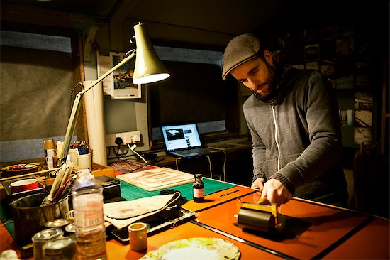 A sign maker rolling ink across the cut raised surface of linoleum preparing to print. Photographie de stock - Premium Libres de Droits, Le code de l’image : 6118-08659696