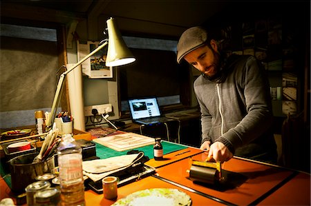 A sign maker rolling ink across the cut raised surface of linoleum preparing to print. Photographie de stock - Premium Libres de Droits, Code: 6118-08659696