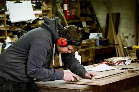A man working in a furniture maker's workshop wearing ear defenders and using a sharp chisel on wood. Stockbilder - Premium RF Lizenzfrei, Bildnummer: 6118-08659749