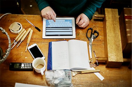 people working at crafts - A person sitting at a workbench, using a digital tablet. Tools, scissors and a smart phone on the desk. Stock Photo - Premium Royalty-Free, Code: 6118-08659721