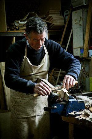 A man working in a furniture maker's workshop, sanding a piece of wood held in a clamp. Stock Photo - Premium Royalty-Free, Code: 6118-08659738