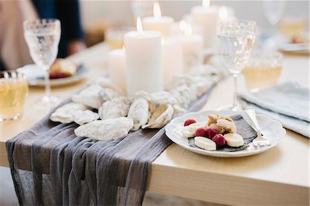 dinner plates on table not people - A table for a celebration meal with wine glasses filled and plates of fruit, and lit candles in the centre of the table. Stock Photo - Premium Royalty-Free, Code: 6118-08659842