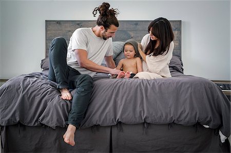 simsearch:6118-08659784,k - A young couple and their young son sitting together on their bed. Foto de stock - Royalty Free Premium, Número: 6118-08659802