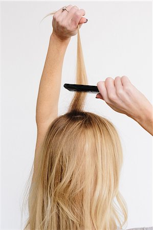 A young woman with long blond wavy hair using a comb. Back view. Stock Photo - Premium Royalty-Free, Code: 6118-08659809