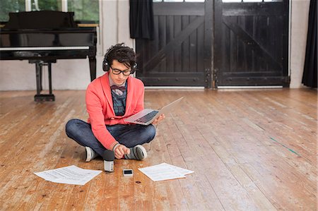 Young man sitting on the floor in a rehearsal studio, using a laptop computer, looking at sheet music. Foto de stock - Sin royalties Premium, Código: 6118-08659951