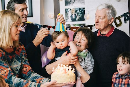 A family gathered to celebrate a one year old girl's birthday party. A cake with lots of candles. Stock Photo - Premium Royalty-Free, Code: 6118-08659997