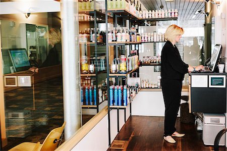 A woman using a laptop in a hair salon, reception, managing the business. Stock Photo - Premium Royalty-Free, Code: 6118-08660002