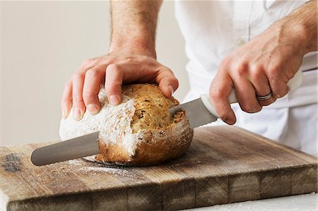 food skills - Close up of a baker slicing a freshly baked loaf of bread with a bread knife. Stock Photo - Premium Royalty-Free, Code: 6118-08660014