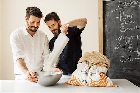 pelle - Two bakers standing at a table, preparing bread dough, adding flour from a paper sack into a metal mixing bowl. Photographie de stock - Premium Libres de Droits, Code: 6118-08660019