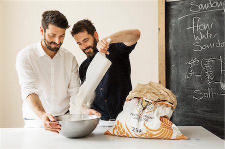 simsearch:6118-08660034,k - Two bakers standing at a table, preparing bread dough, adding flour from a paper sack into a metal mixing bowl. Stock Photo - Premium Royalty-Free, Code: 6118-08660019