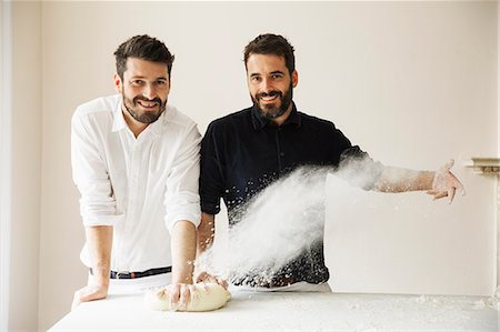 Two bakers standing at a table, kneading bread dough, dusting it with flour. Fotografie stock - Premium Royalty-Free, Codice: 6118-08660021