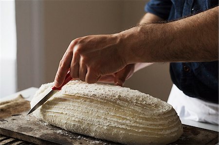 Close up of a baker slicing a freshly baked loaf of bread with a bread knife. Stock Photo - Premium Royalty-Free, Code: 6118-08660027
