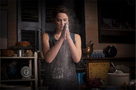 spalmare (applicare) - Valentine's Day baking, young woman standing in a kitchen, rubbing flour between her hands. Fotografie stock - Premium Royalty-Free, Codice: 6118-08660165