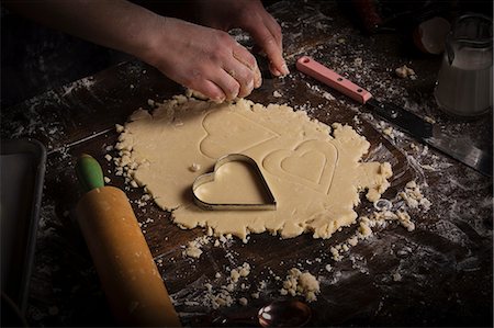 simsearch:6118-08660146,k - Valentine's Day baking. Woman cutting out heart shaped biscuits from dough on a floured surface. Stock Photo - Premium Royalty-Free, Code: 6118-08660186