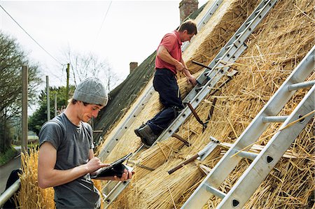 Two thatchers thatching a roof, one using a digital tablet the other standing on a ladder. Foto de stock - Sin royalties Premium, Código: 6118-08660199