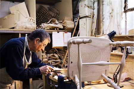 simsearch:6118-08660112,k - Man standing at a work bench in a carpentry workshop, working on a wooden chair. Foto de stock - Royalty Free Premium, Número: 6118-08660101