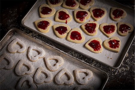 simsearch:6118-08660146,k - Valentine's Day baking, woman spreading raspberry jam on heart shaped biscuits. Stock Photo - Premium Royalty-Free, Code: 6118-08660135