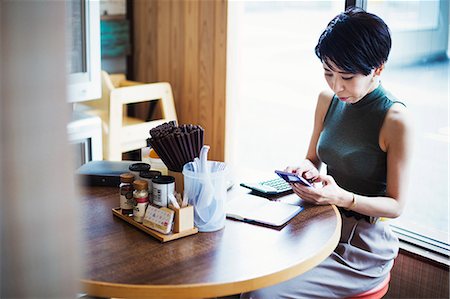 fast food city - The ramen noodle shop. A woman sitting at a table using her smart phone. Stock Photo - Premium Royalty-Free, Code: 6118-08761690